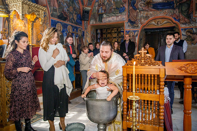 Отецът кръщава момиче в купела по време на ритуал Свето Кръщение в Кукленски манастир Св. Св. Козма и Дамян.