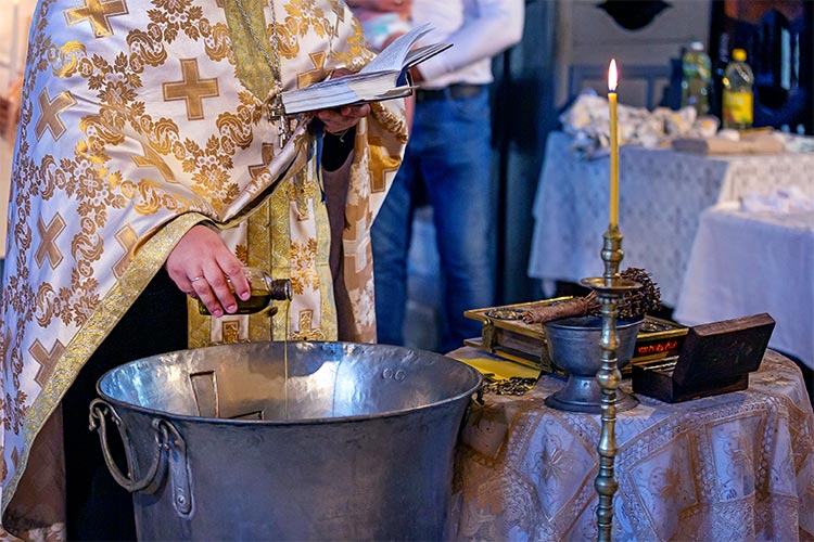 Отецът освещава водата в купела по време на ритуал Свето Кръщение.