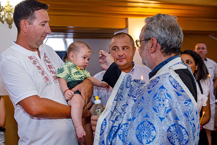 Отецът помазва момченцето по челцето преди кръщаването в купела.