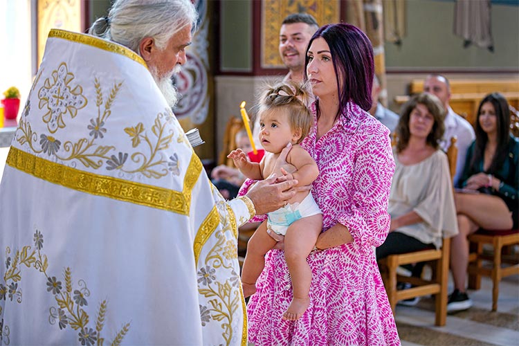 Отецът помазва момиченцето по ръчичката преди кръщаването в купела.