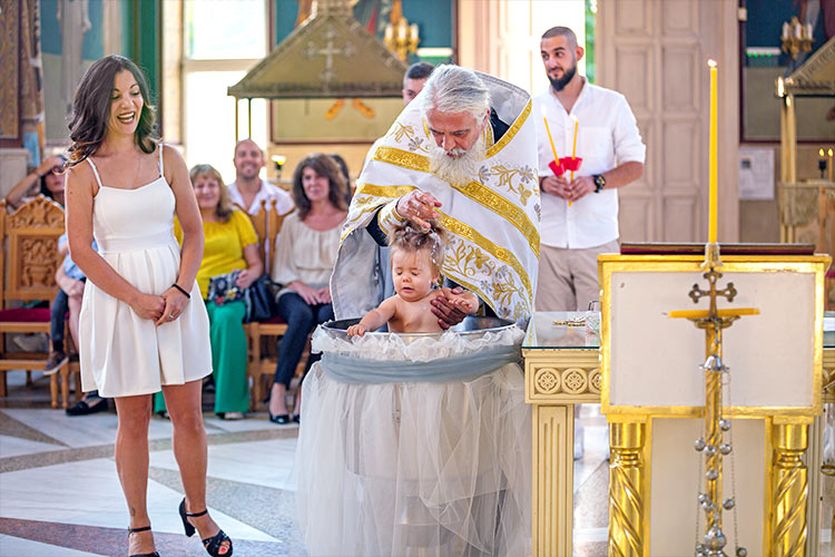 Отецът кръщава момиченце в купела по време на ритуал Свето Кръщение в храм Свети Николай Мирликийски Чудотворец, град Пловдив.