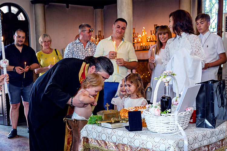 Отецът кръщава момиченце в купела по време на ритуал Свето Кръщение в храм Света Троица, Кръстова Гора.