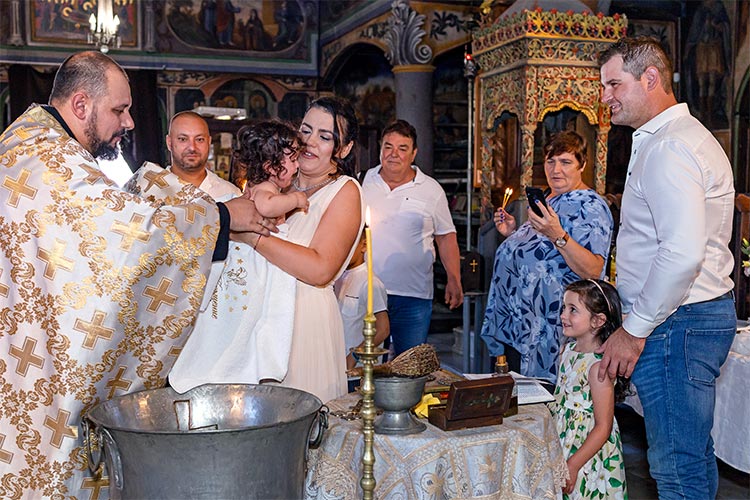 Майката приема момиченцето след кръщаването в купела от отеца по време на ритуал Свето Кръщение в храм Свети Свети Константин и Елена, град Пловдив.