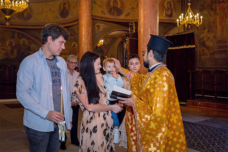 Отецът възлага ръка върху главата на момченцето по време на ритуал Свето Кръщение в катедрален храм Света Богородица, град Пловдив.